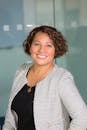 A confident woman with curly hair smiling in an office environment, conveying professionalism and approachability.